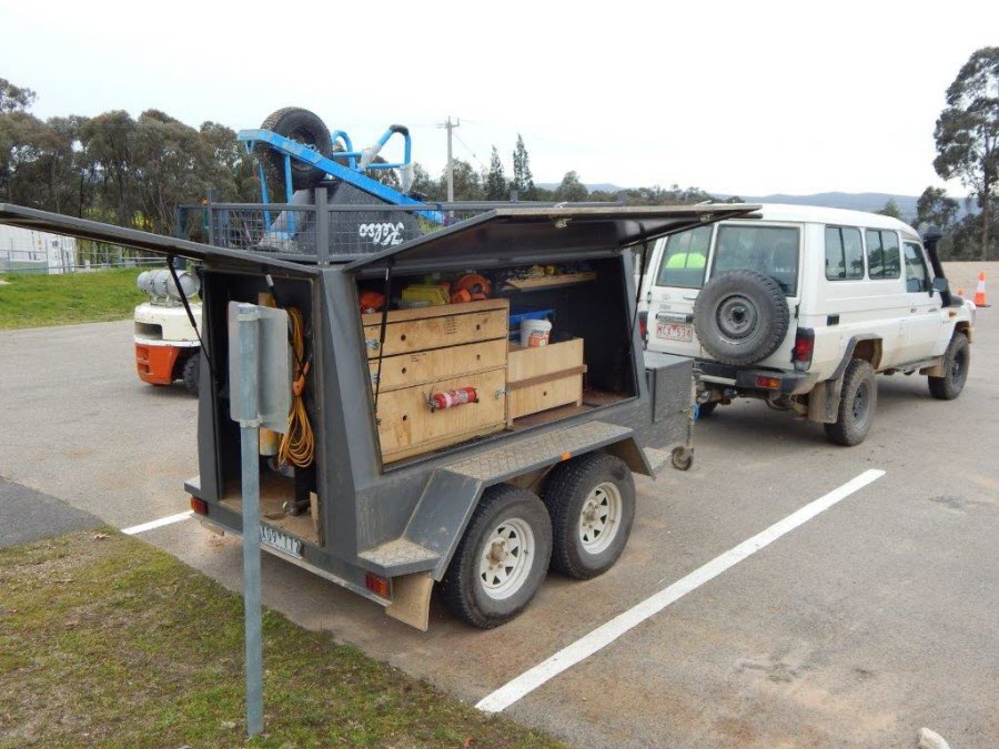 Landmate white 4WD vehicle and trailer with tools and gear.